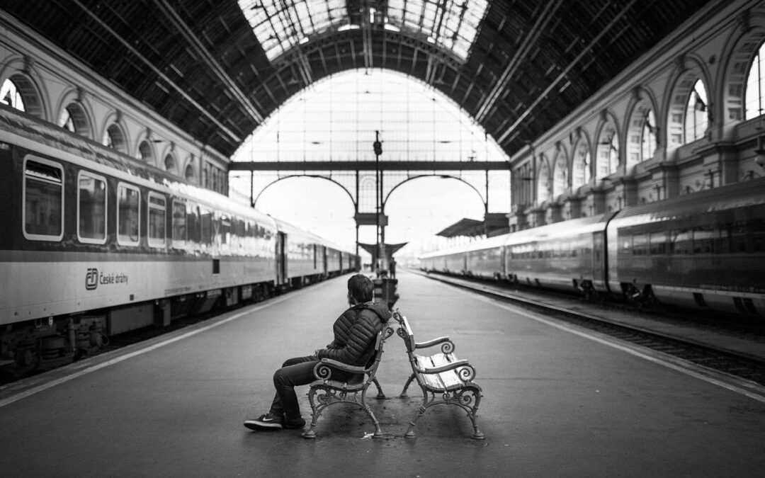 Imagen en blanco y negro de un hombre solo, sentado en una estación de tren.